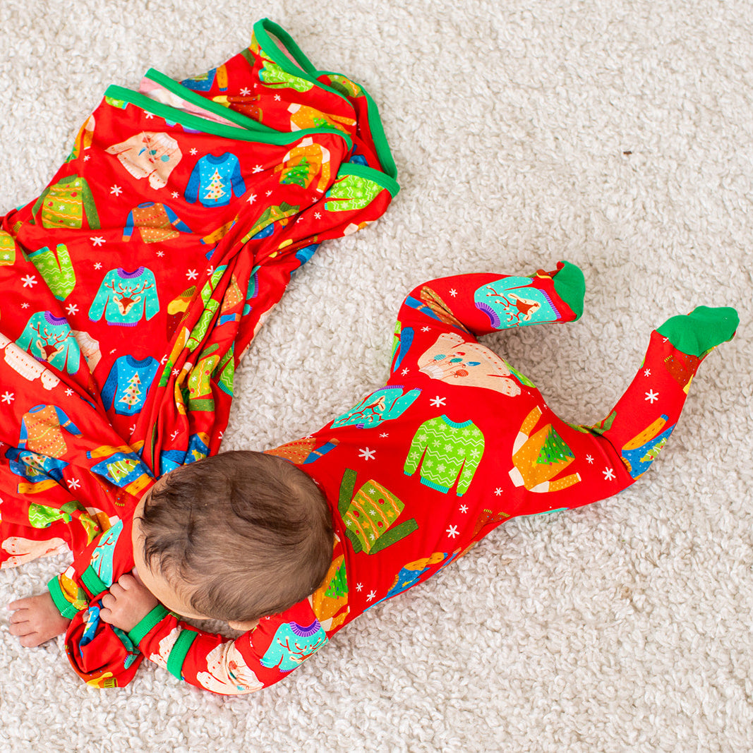 Baby wearing a red Christmas-themed onesie on a light-colored carpet