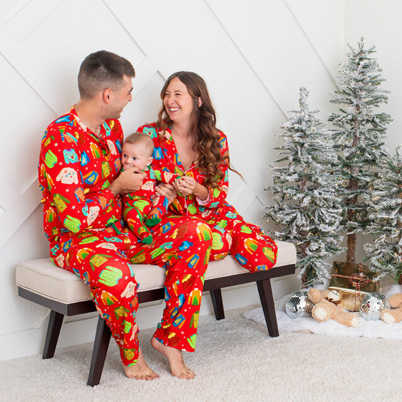 Family in matching pajamas sitting on a bench with a Christmas tree and gifts in the background.
