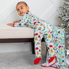 Child wearing a colorful onesie with animal patterns, sitting on a bench next to a Christmas tree.