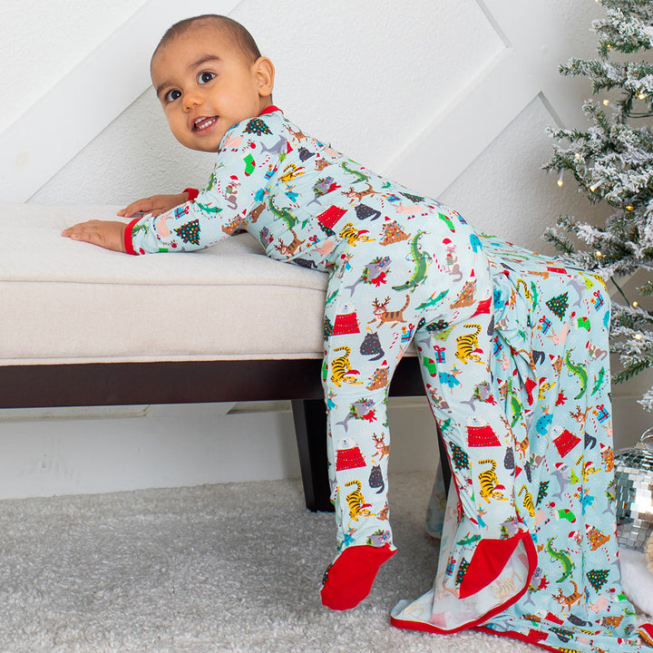 Child wearing a colorful onesie with animal patterns, sitting on a bench next to a Christmas tree.