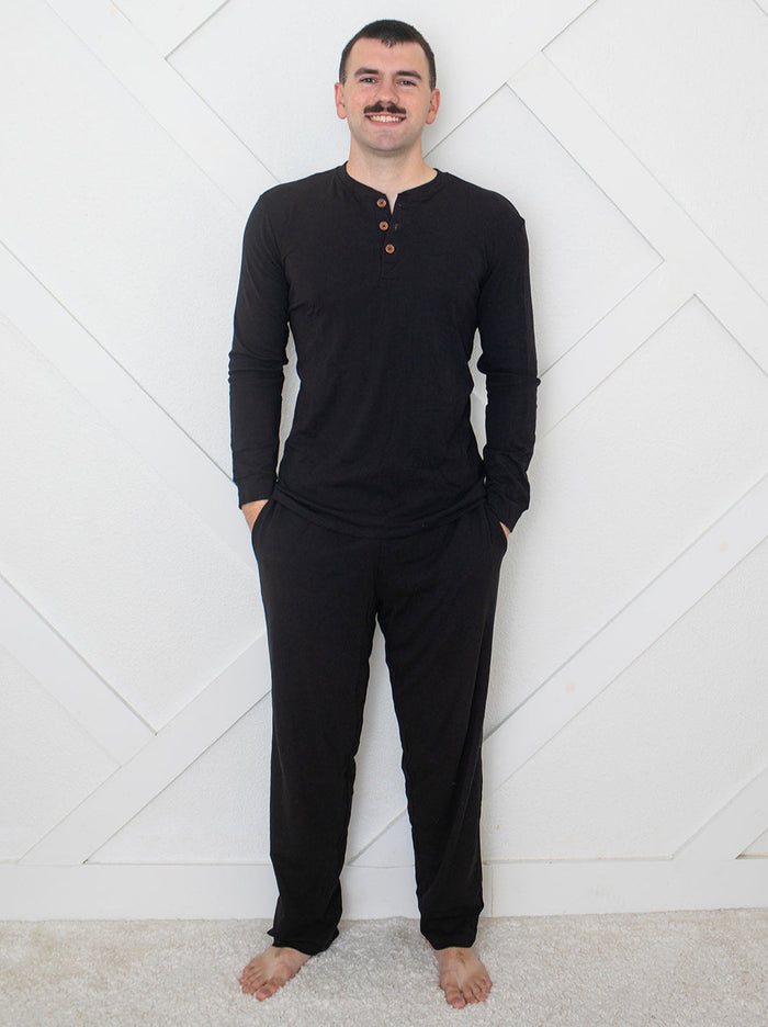 Man wearing a black long-sleeve shirt and pants against a white geometric-patterned wall.