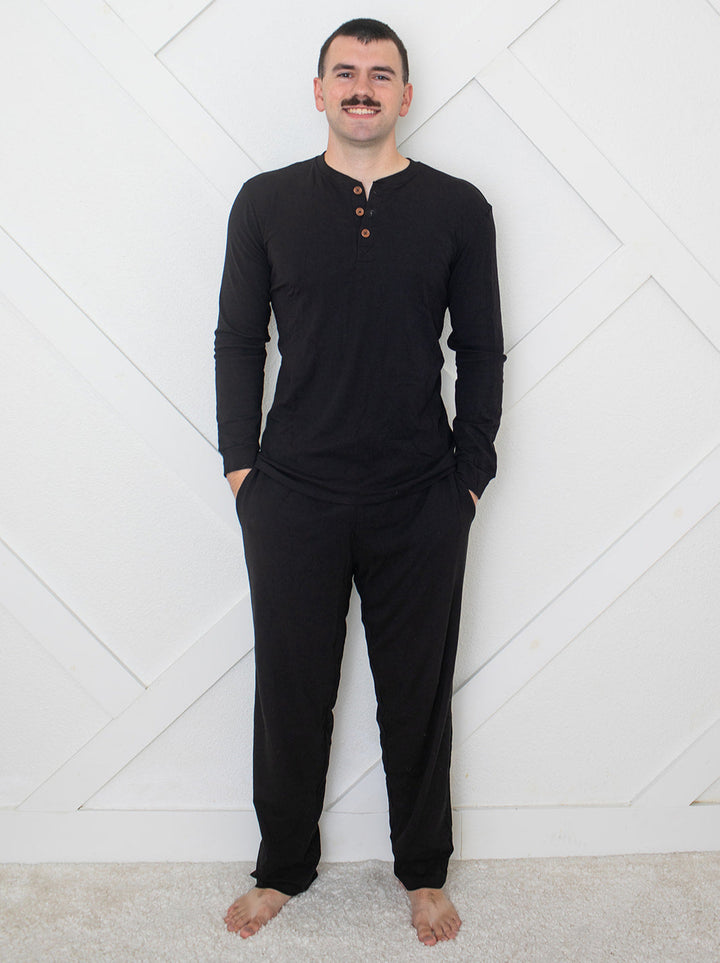 Man wearing a black long-sleeve shirt and pants against a white geometric-patterned wall.