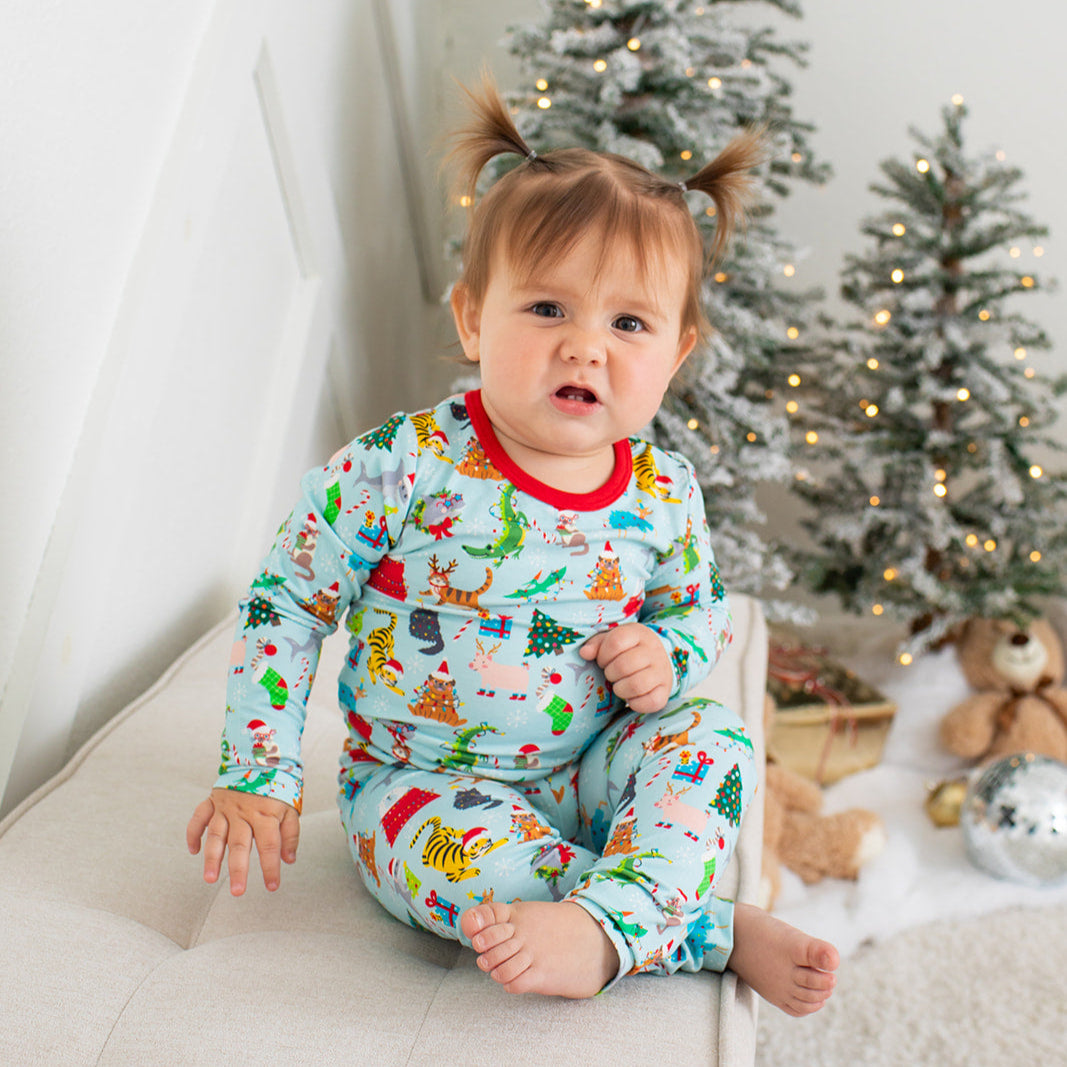 Baby in festive pajamas sitting on a couch with Christmas trees in the background