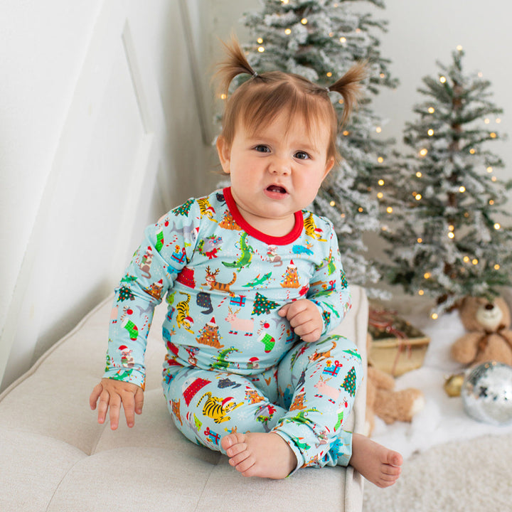 Baby in festive pajamas sitting on a couch with Christmas trees in the background