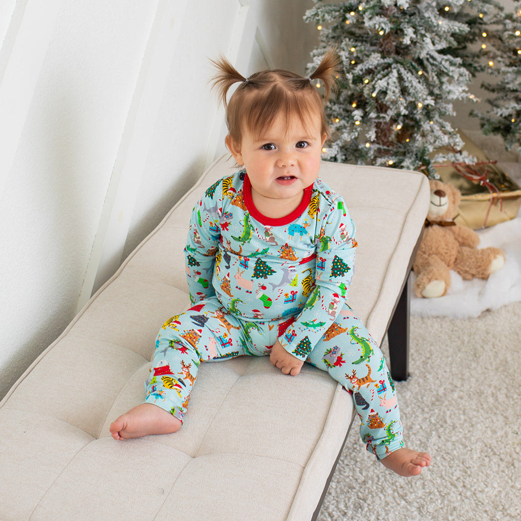 Child wearing festive pajamas sitting on a chair with a decorated Christmas tree in the background