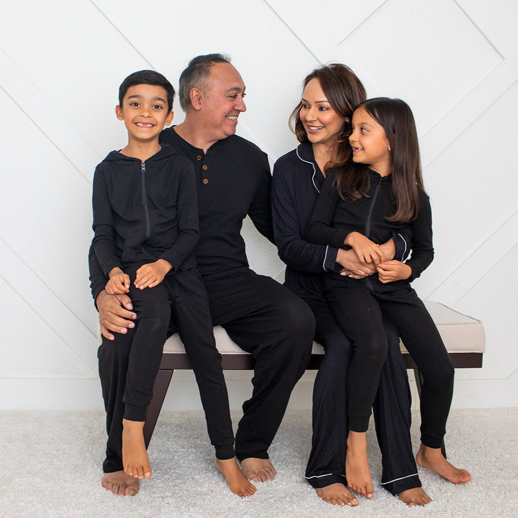 Family of four sitting on a bench against a white geometric patterned wall.