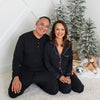 Man and woman in matching pajamas sitting on the floor in front of a decorated Christmas tree.