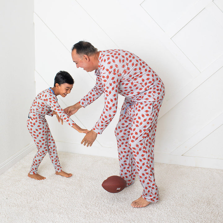 Man and child in matching pajamas playing with a football on a white floor.