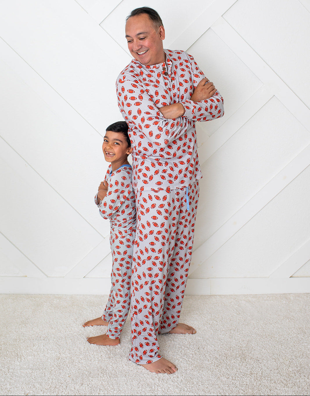 Man and child wearing matching red polka dot pajamas against a white geometric patterned wall.