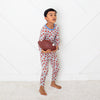 Child in red and white patterned pajamas holding a brown football on a white floor.