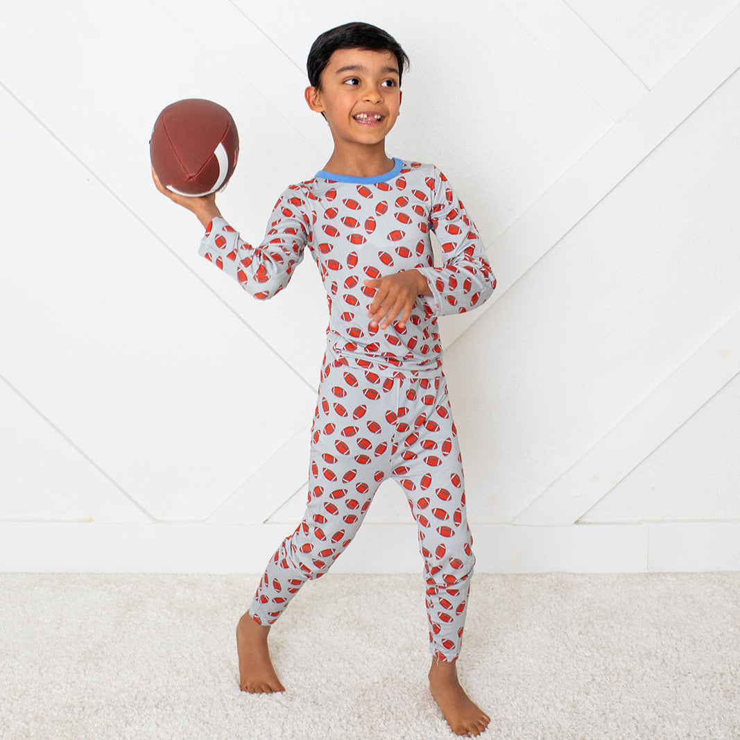 Child in red and white polka dot pajamas holding a football on a white background