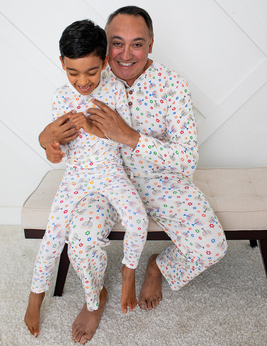 Man and child sitting on a bench wearing matching pajamas with a white background