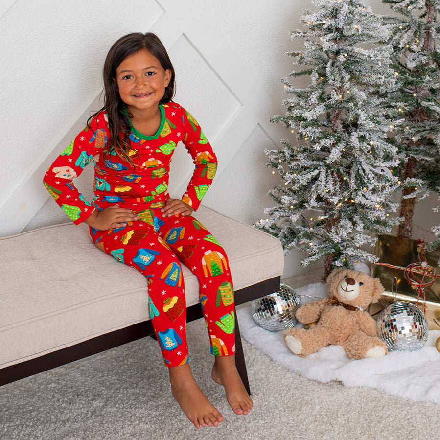 Child in red Christmas pajamas sitting on a couch next to a decorated Christmas tree.