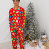 Person wearing a red Christmas-themed pajama set standing next to a decorated tree with ornaments and a teddy bear.