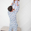 Man and child in matching blue floral pajamas against a white geometric-patterned wall.