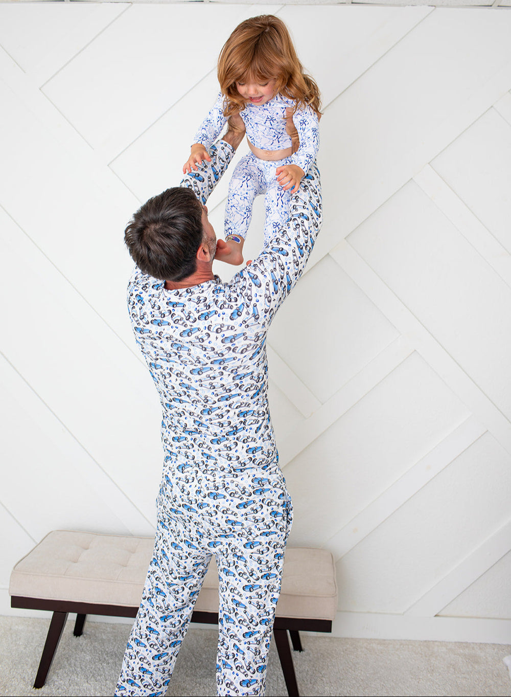 Man and child in matching blue floral pajamas against a white geometric-patterned wall.