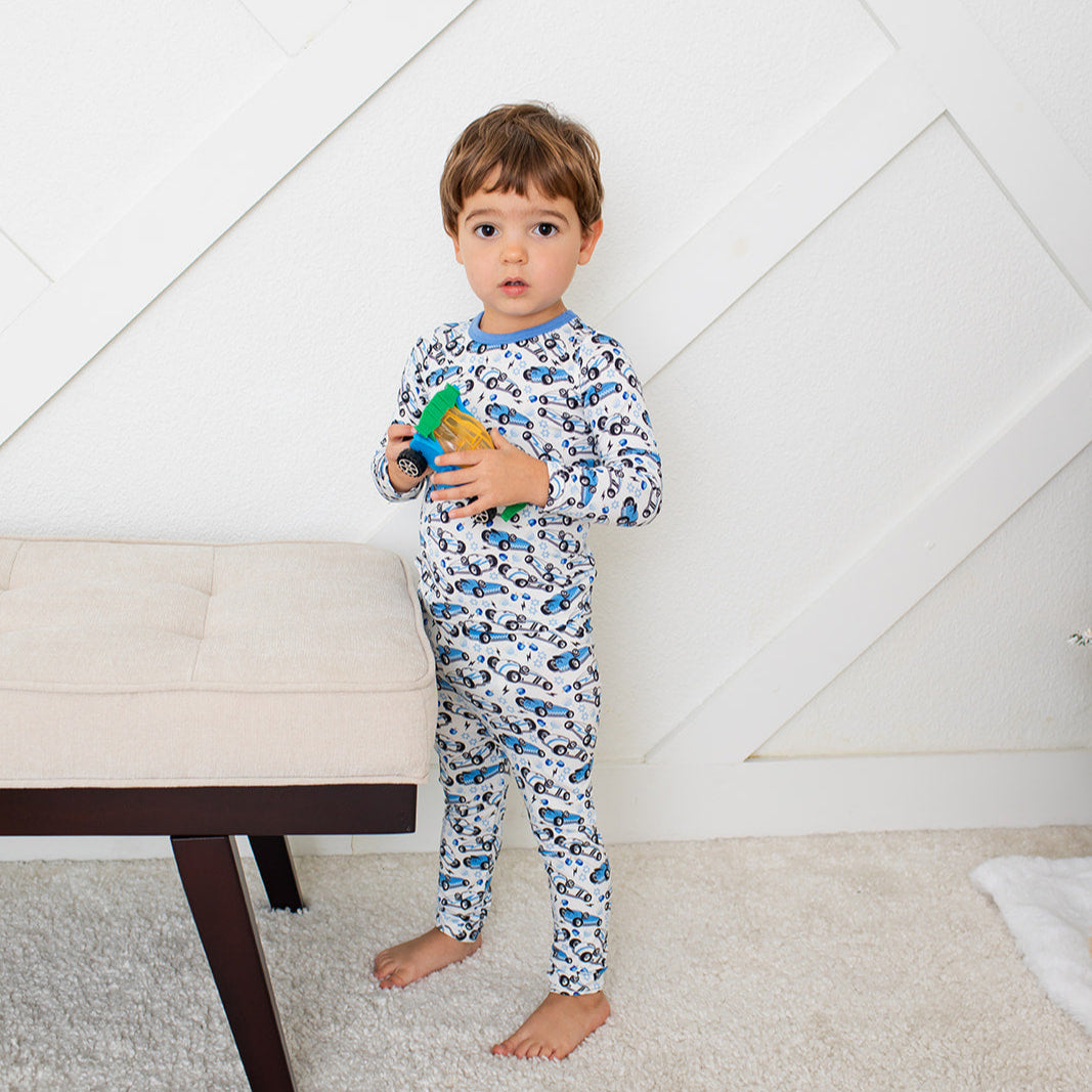 Child in pajamas holding a toy in a room with a white wall and carpeted floor.