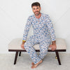 Man wearing a blue patterned pajama set sitting on a bench against a white wall.
