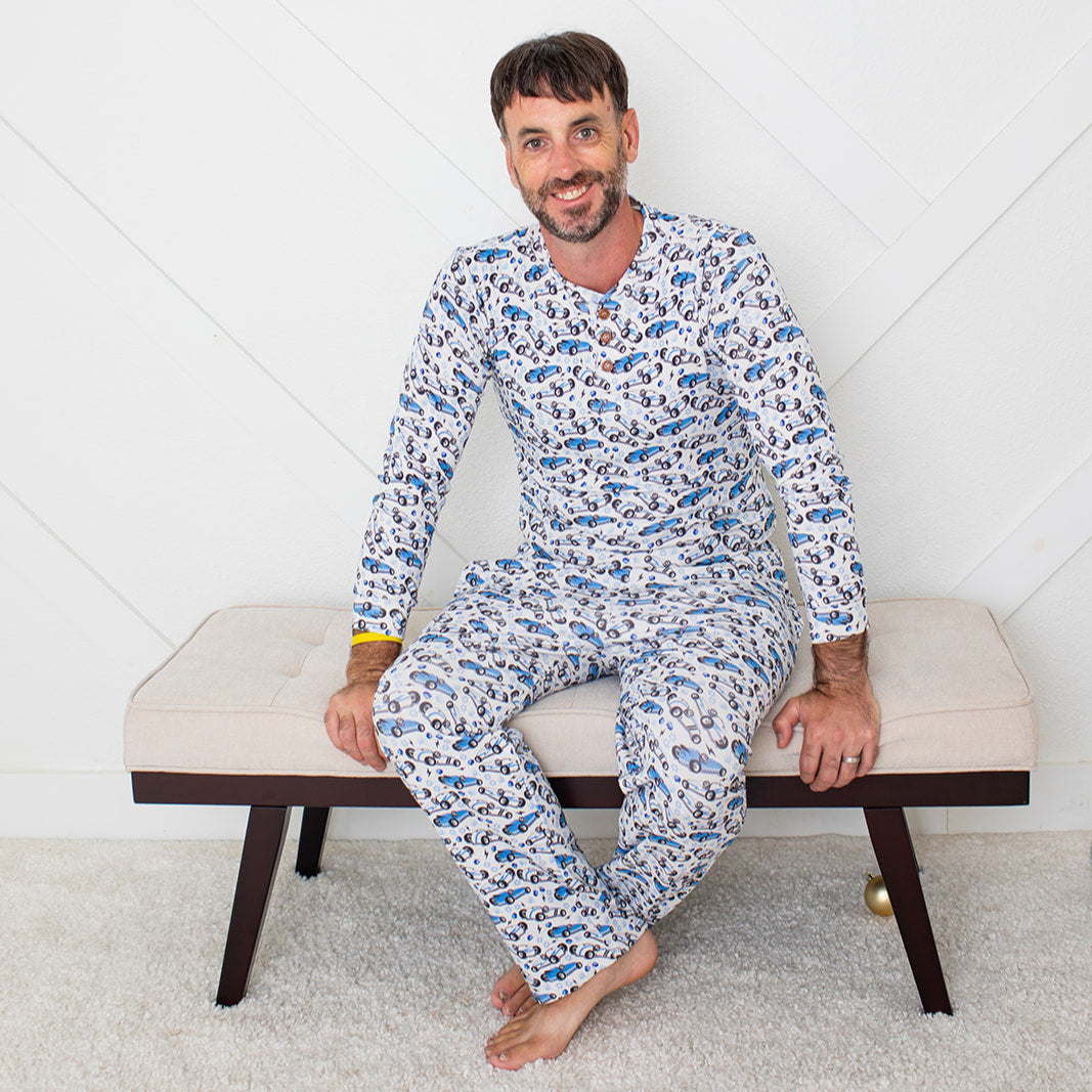 Man wearing a blue patterned pajama set sitting on a bench against a white wall.