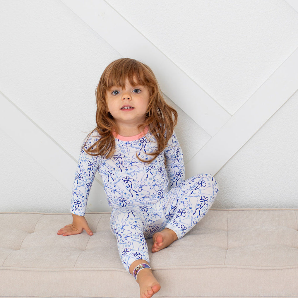 Child wearing a floral pajama set sitting on a beige couch against a white wall.