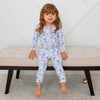 Child wearing a blue floral onesie sitting on a beige bench.