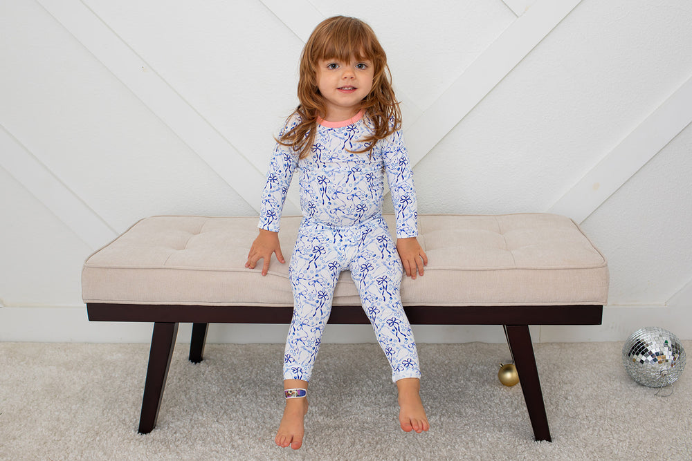 Child wearing a blue floral onesie sitting on a beige bench.