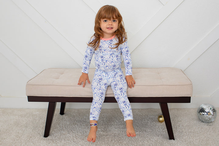 Child wearing a blue floral onesie sitting on a beige bench.