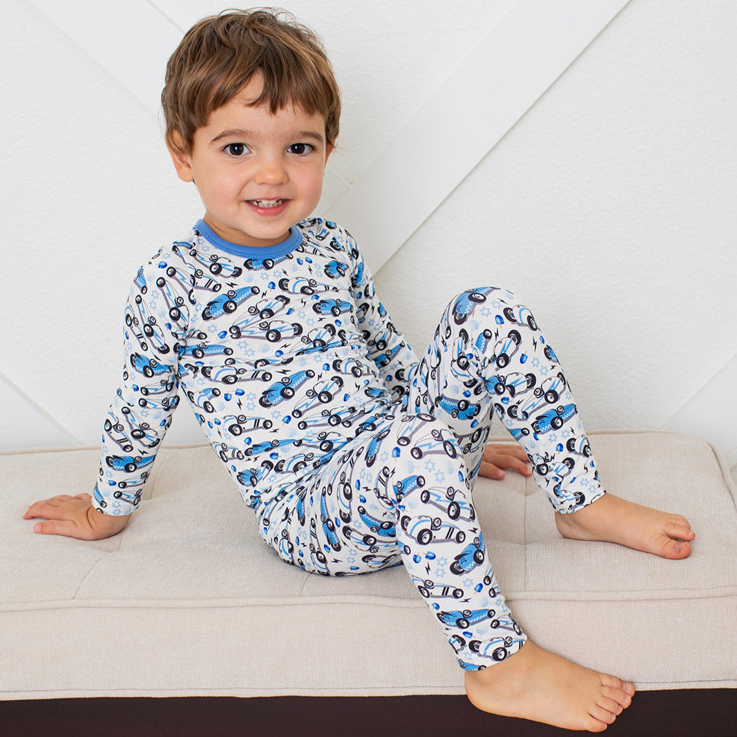 Child wearing a car-patterned pajama set sitting on a bench.