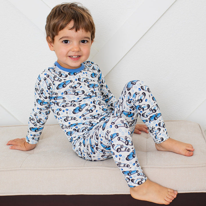 Child wearing a car-patterned pajama set sitting on a bench.