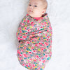 Baby swaddled in a colorful floral blanket on a white background