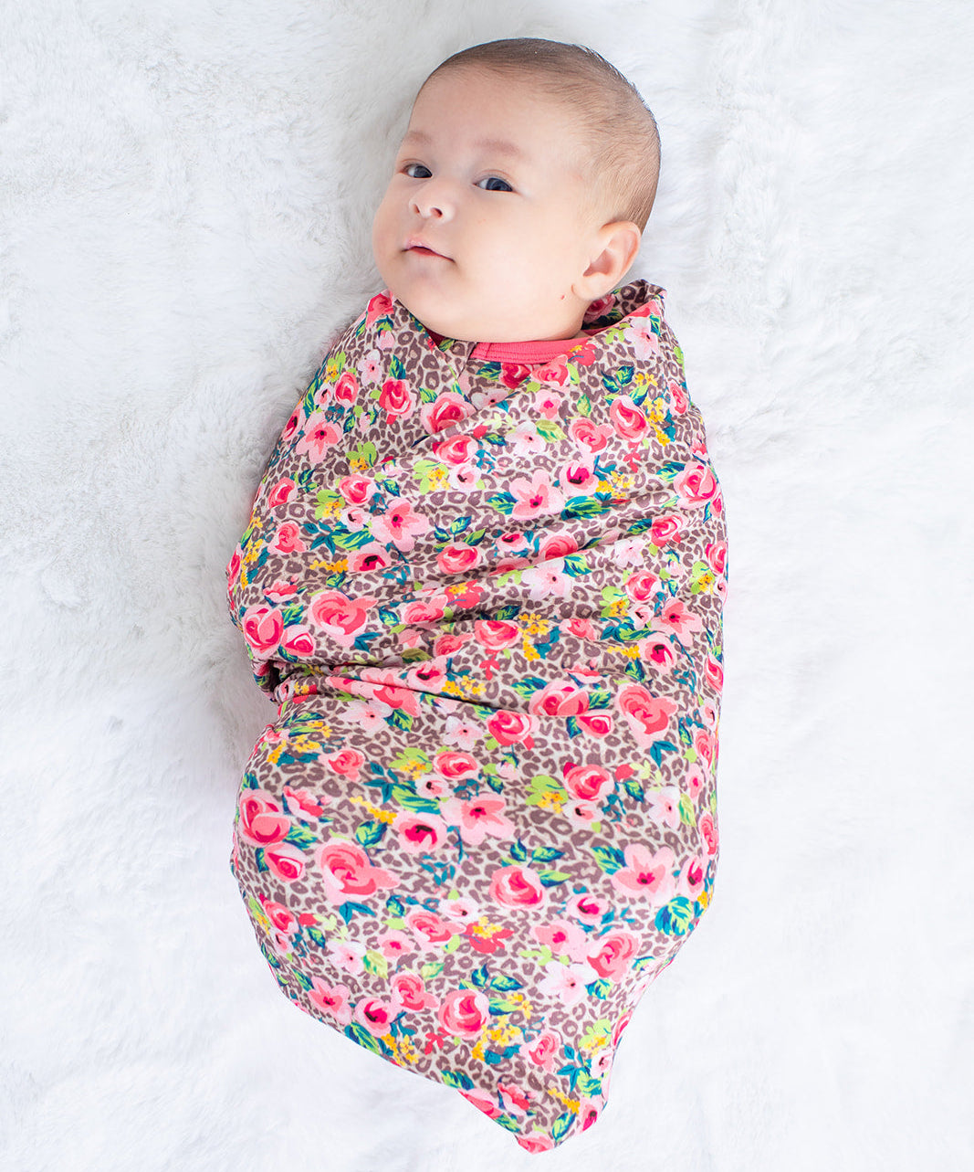 Baby swaddled in a colorful floral blanket on a white background
