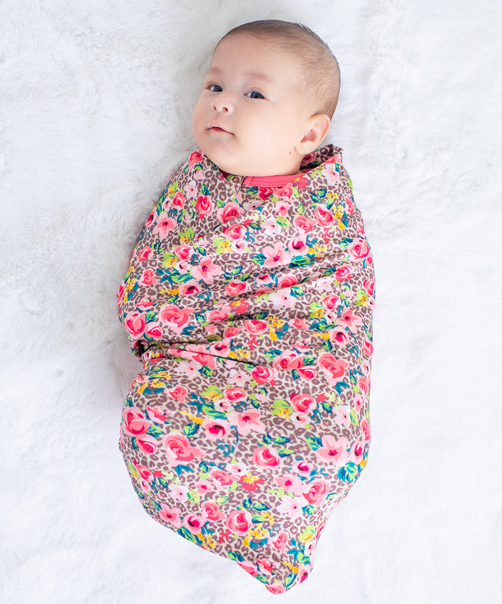 Baby swaddled in a colorful floral blanket on a white background