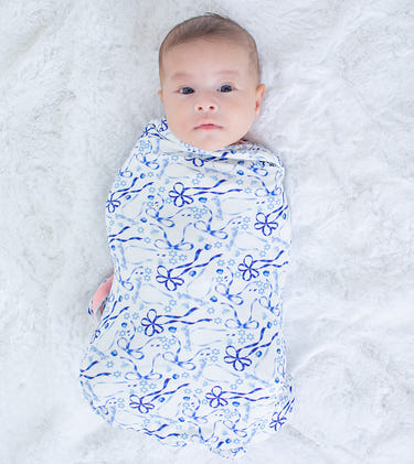 Baby swaddled in a blue floral pattern on a white blanket