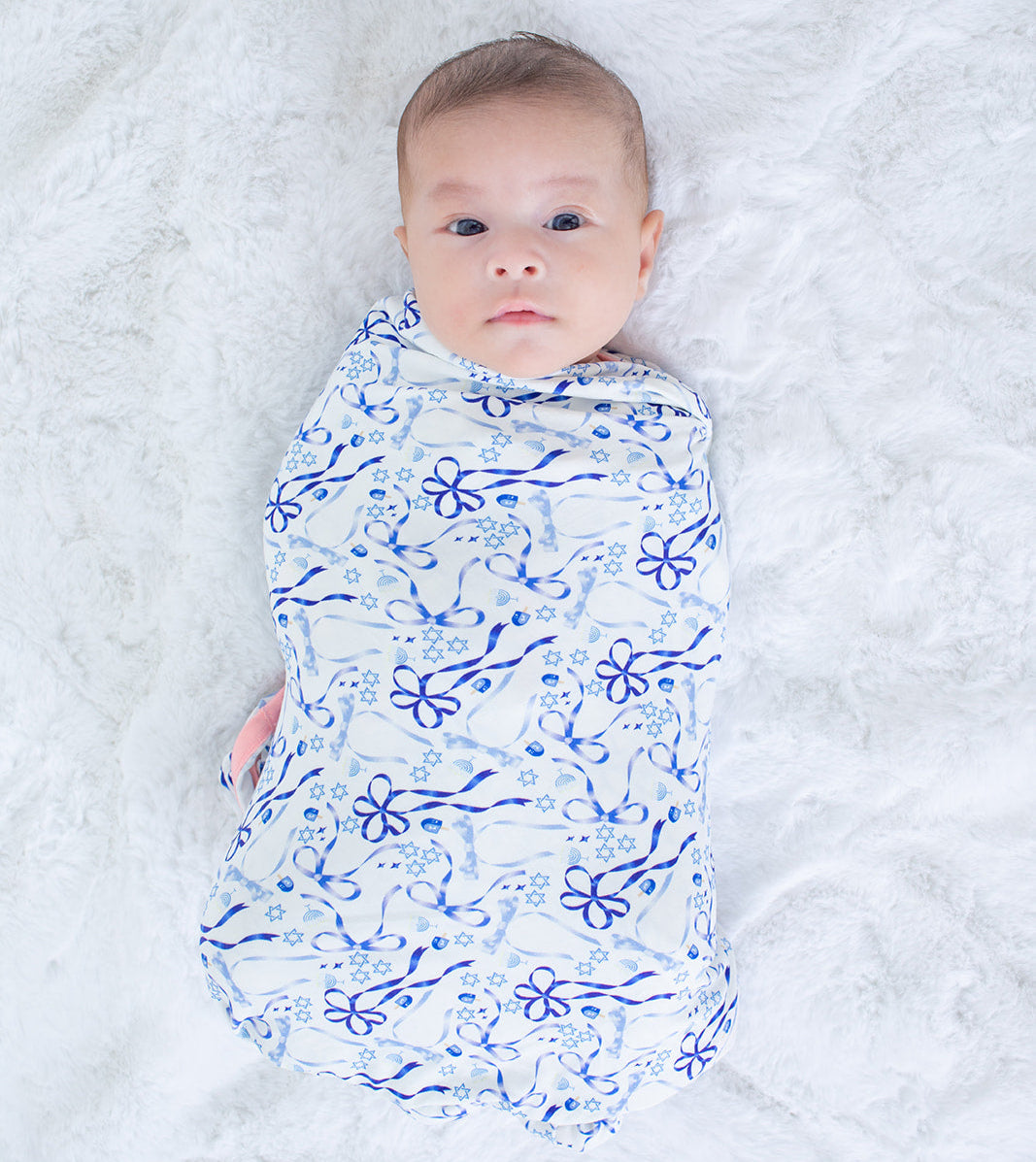 Baby swaddled in a blue floral pattern on a white blanket