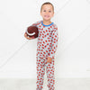 Child wearing a patterned onesie holding a football on a white background