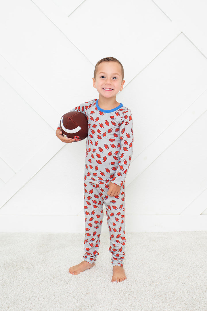 Child wearing a patterned onesie holding a football on a white background