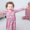 Child wearing a floral nightgown with a woman in the background, both on a carpeted floor.