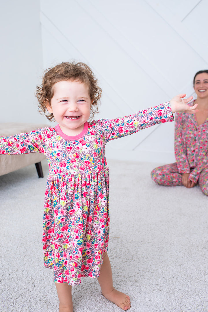 Child wearing a floral nightgown with a woman in the background, both on a carpeted floor.