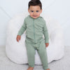 Child wearing a green outfit sitting on a white bean bag chair with a toy train on a light gray floor.