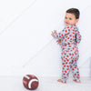 Child in a patterned onesie standing next to a football on a white floor.