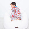 Child in a patterned onesie sitting on a white bean bag chair against a light gray background