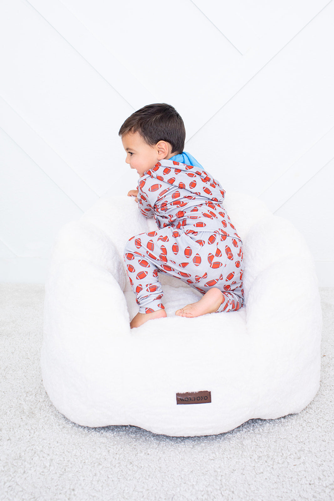 Child in a patterned onesie sitting on a white bean bag chair against a light gray background