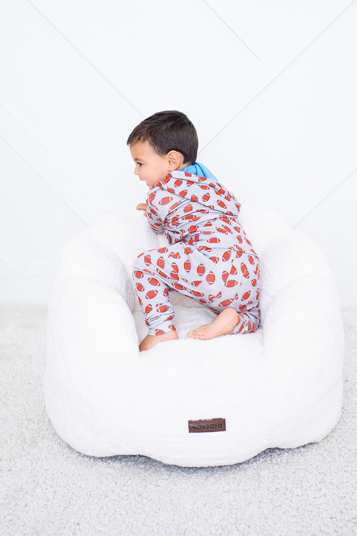 Child in a patterned onesie sitting on a white bean bag chair against a light gray background