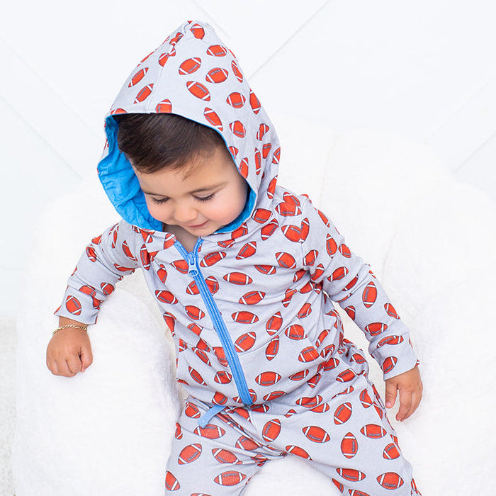 Child wearing a red and white patterned onesie sitting on a bean bag chair.