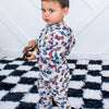 Child wearing a colorful car-patterned onesie on a checkered rug.