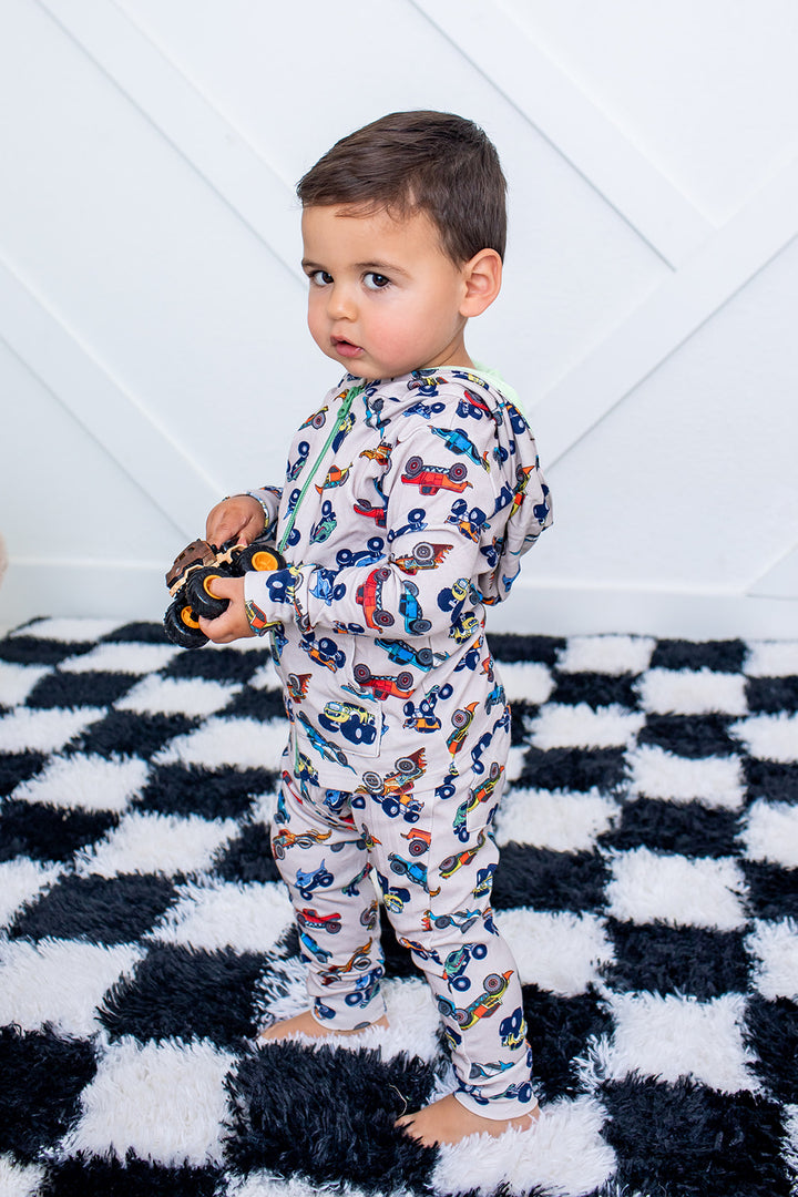 Child wearing a colorful car-patterned onesie on a checkered rug.