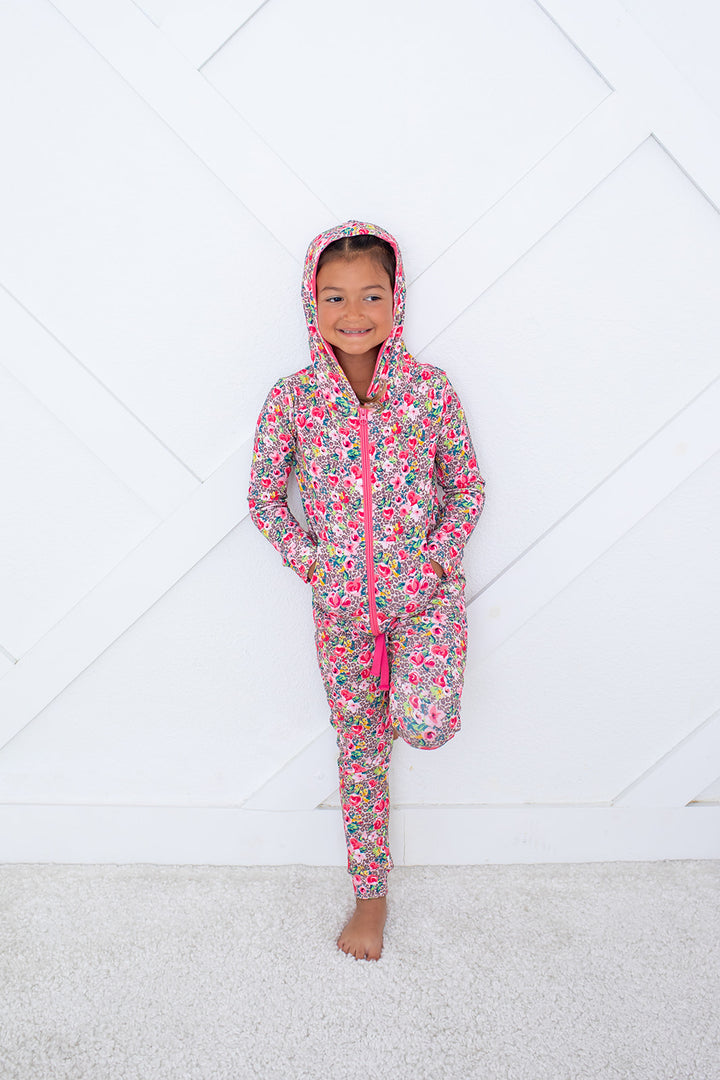 Child wearing a floral onesie with pink zipper on a white floor.