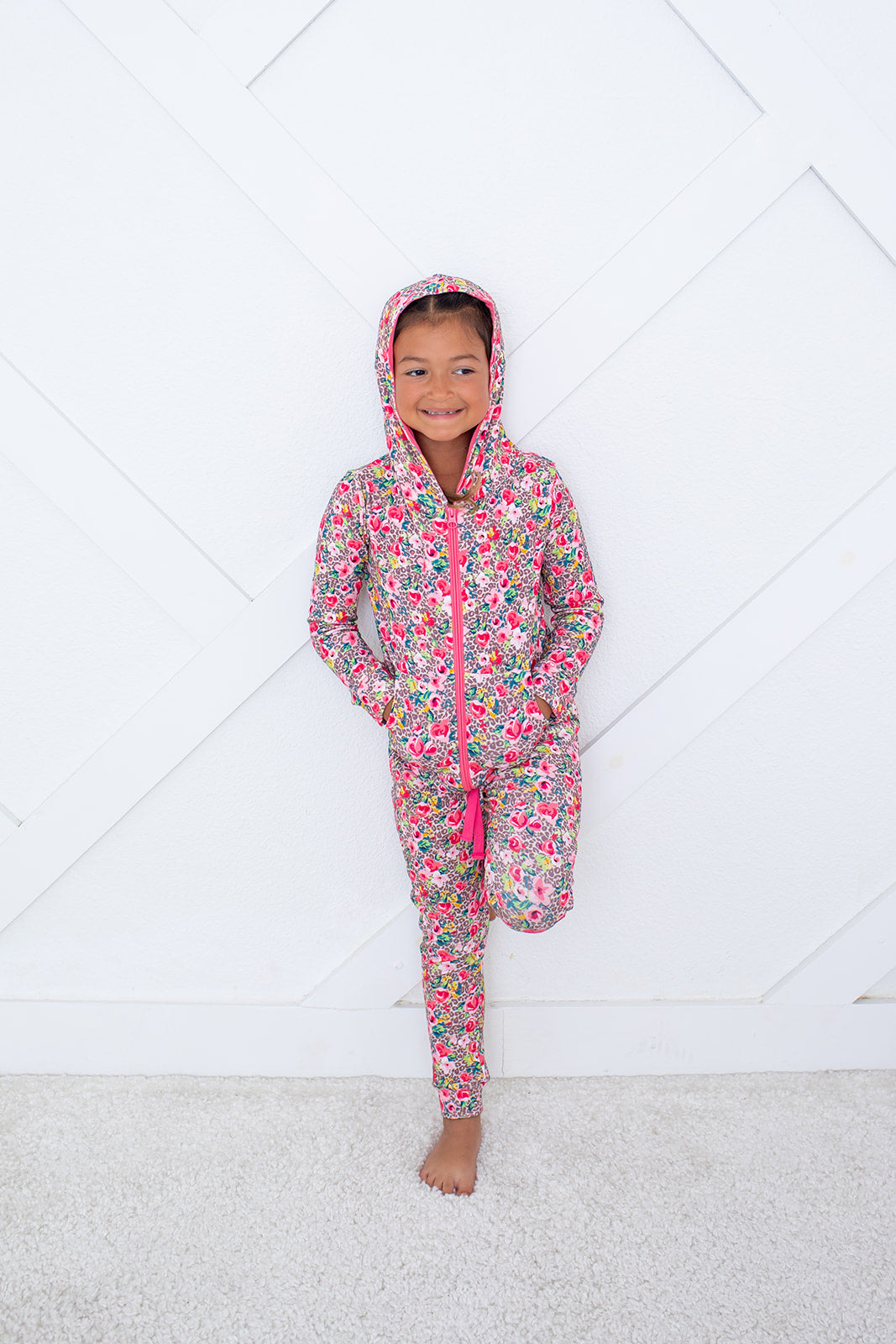 Child wearing a floral onesie with pink zipper on a white floor.