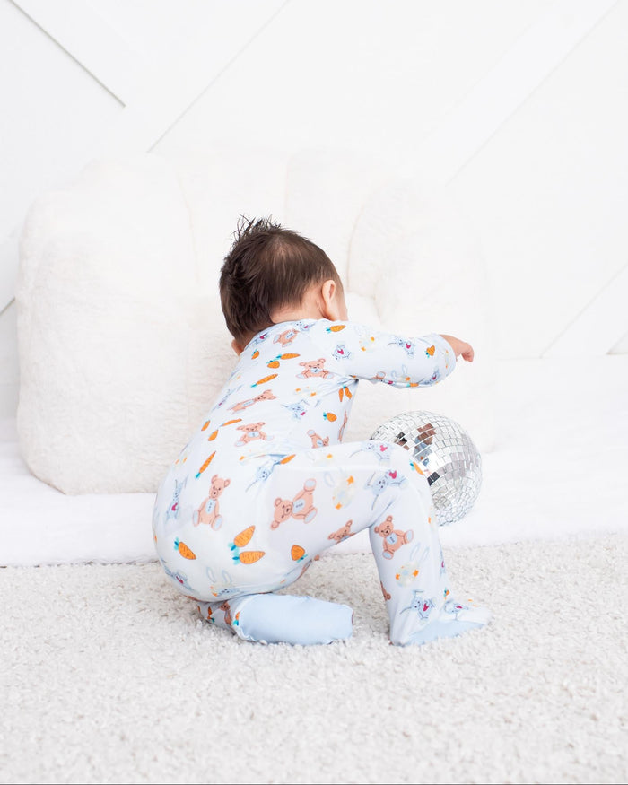 A baby wearing a light blue and white patterned footed pajama set crawls on a white carpet in a bright, modern nursery.