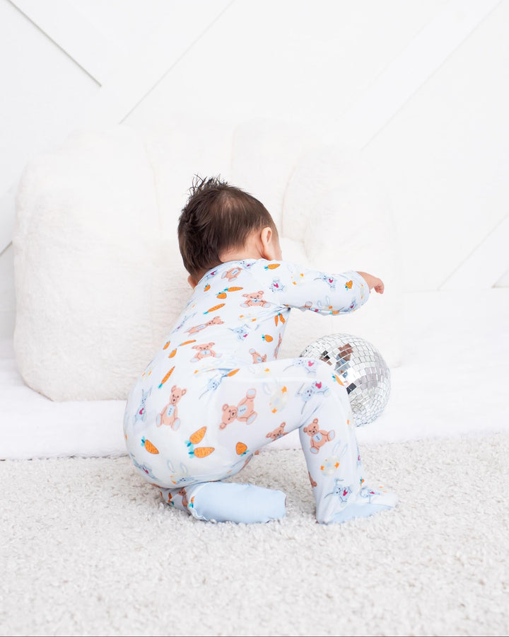 A baby wearing a light blue and white patterned footed pajama set crawls on a white carpet in a bright, modern nursery.